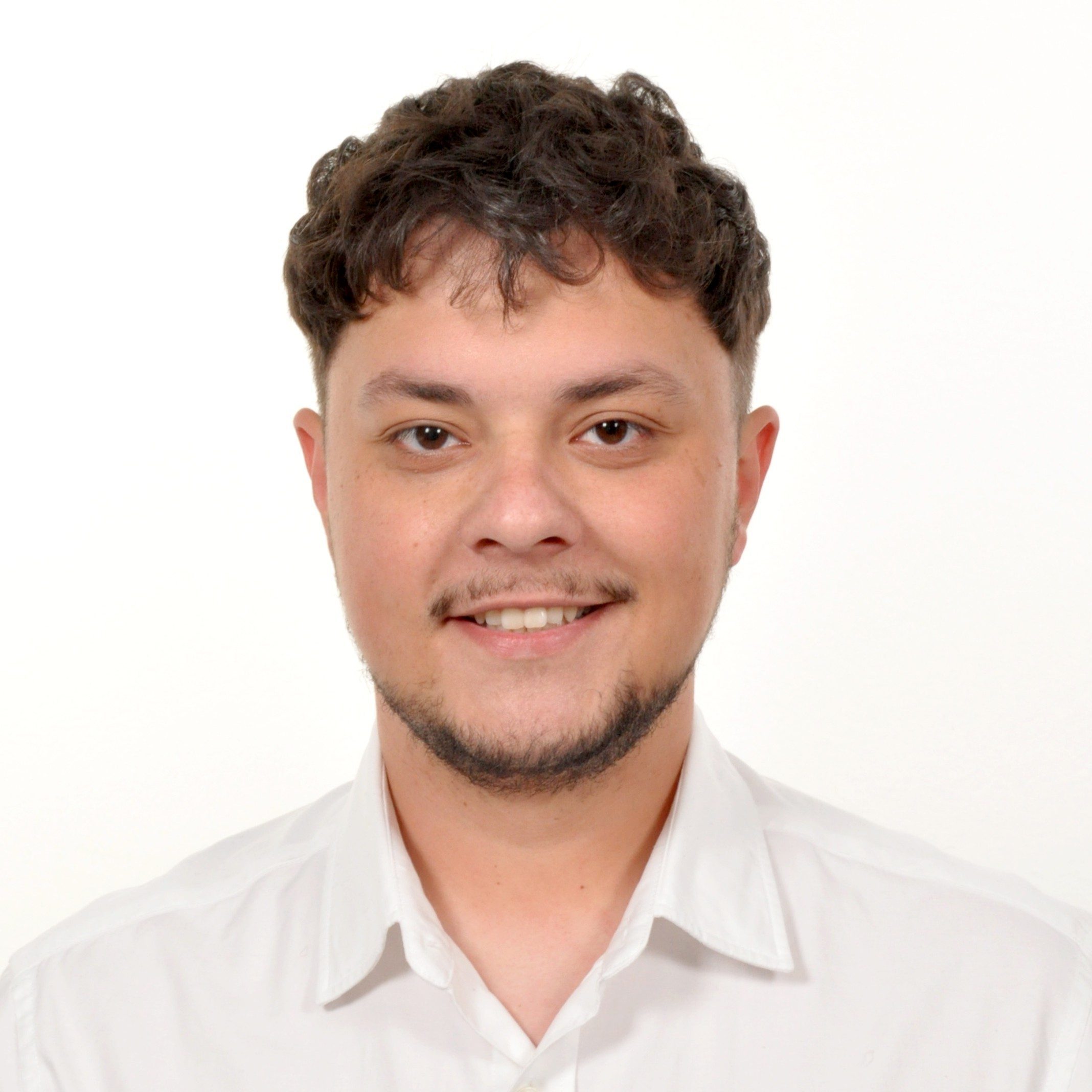 Smiling young man with short curly hair and a trimmed beard wearing a white collared shirt.